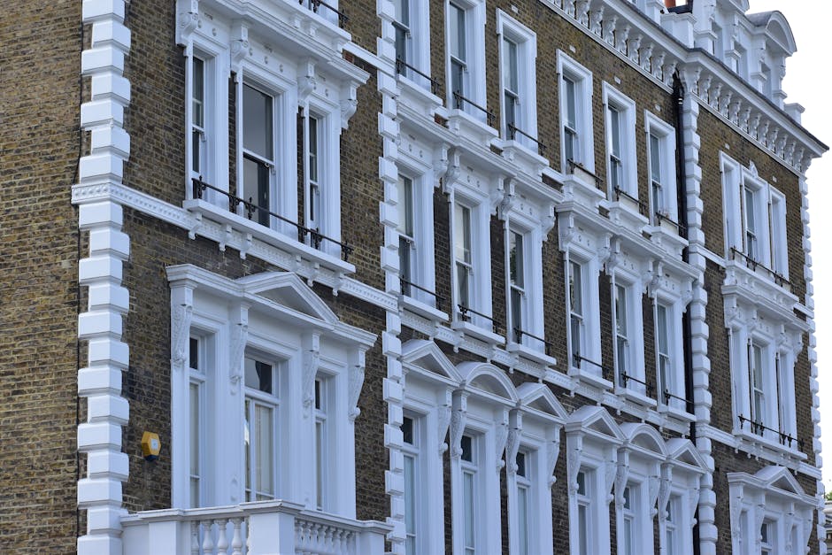 Photograph of a Victorian-style residential building with dark brick exterior and ornate white decorative trim. The facade features multiple large sash windows with white frames and decorative pediments, each with black wrought-iron balconies. The building's detailed architectural elements include cornices and pilasters, highlighted by natural daylight. The overall appearance is clean and well-maintained, emphasizing the building's historic aesthetic. This image aligns with the concept of surface cleaning and maintenance for property hygiene, as promoted by Carpet Cleaners W9, experts in deep cleaning and sanitisation services for homes and commercial buildings in the Maida Vale area.